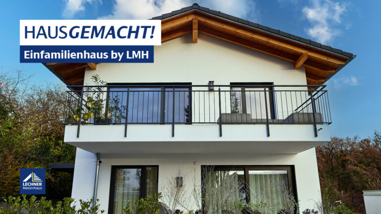 Vorderansicht eines modernen weißen Einfamilienhauses von LMH Lechner Massivhaus, mit einem großen Balkon im Obergeschoss und freiliegenden Holzsparren unter dem Dachgiebel. Über dem Bild steht der Schriftzug "HAUSGEMACHT! Einfamilienhaus by LMH".