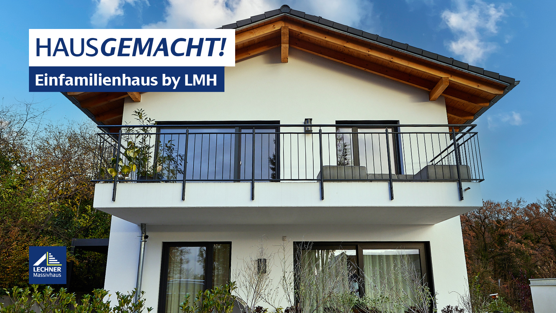 Vorderansicht eines modernen weißen Einfamilienhauses von LMH Lechner Massivhaus, mit einem großen Balkon im Obergeschoss und freiliegenden Holzsparren unter dem Dachgiebel. Über dem Bild steht der Schriftzug "HAUSGEMACHT! Einfamilienhaus by LMH".