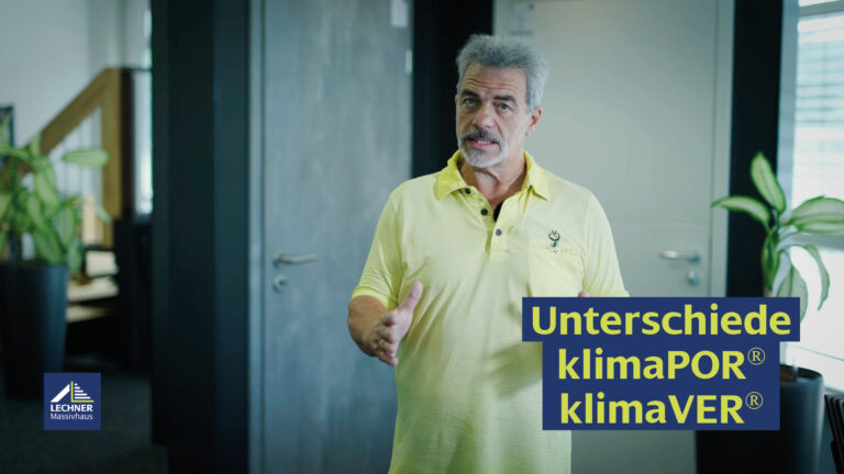 Älterer Mann mit grauem Haar und Bart, gekleidet in ein gelbes Polo-Shirt, erklärt in einem modernen Büro die Unterschiede klimaPOR® klimaVER® von Lechner Massivhaus.