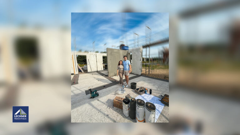 Glückliches Paar vor der Baustelle ihres Massivhauses (Rohbau) von Lechner Massivhaus unter blauem Himmel. Im Vordergrund liegen Baupläne, Dämmrollen und Werkzeug, was den Baufortschritt und die Phase der Bodenplatten-Abdichtung hervorhebt.