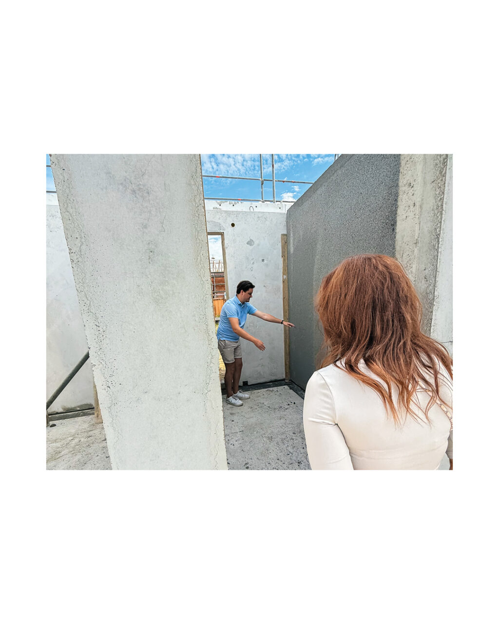 Bauherr im Innenbereich des Rohbaus zeigt der Bauherrin eine fertig montierte Betonwand oder Fertigteilwand. Das Bild zeigt die Wandmontage und das Raumgefühl im frühen Hausbau.