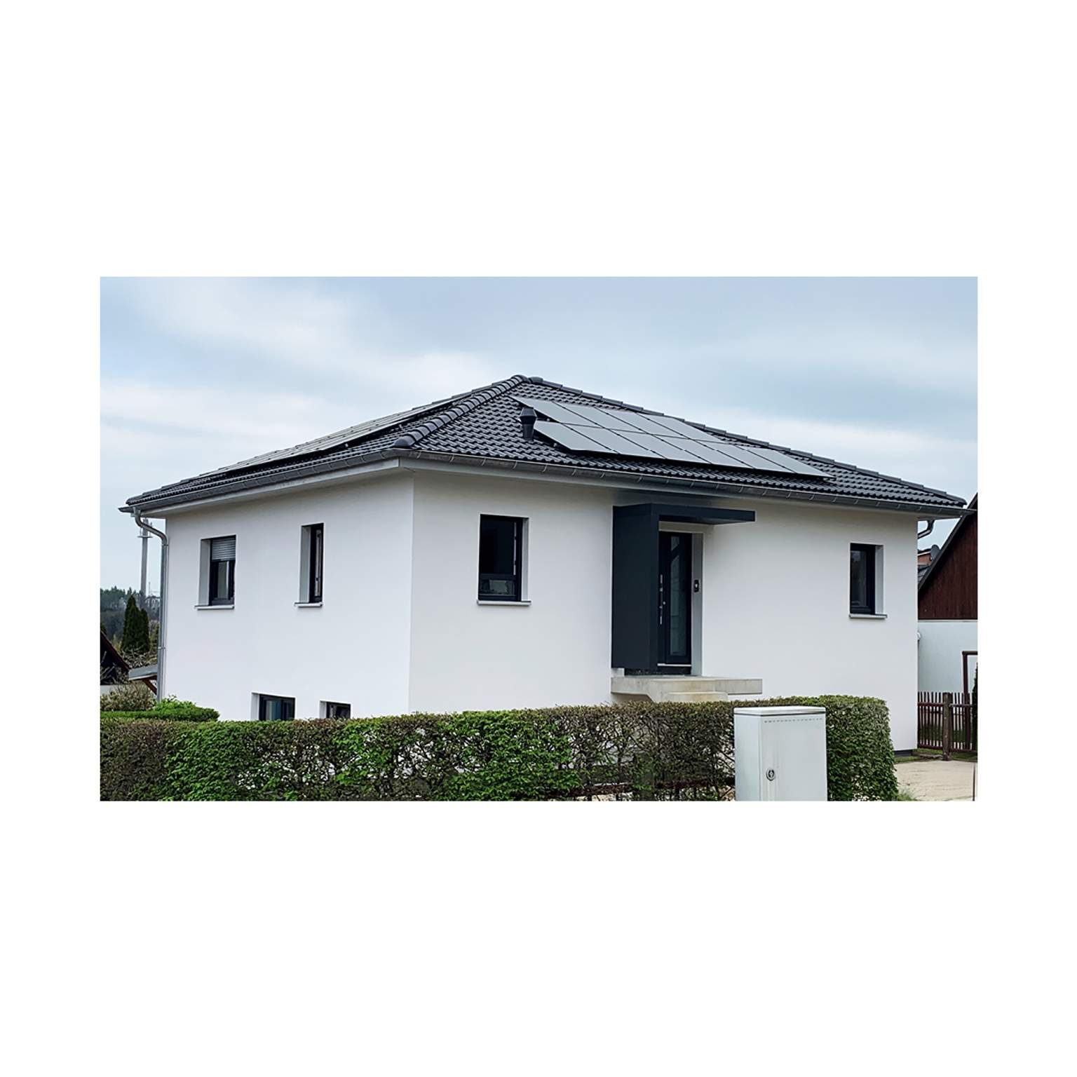 Bungalow-Stil Massivhaus mit Walmdach und moderner PV-Anlage auf dem Dach.