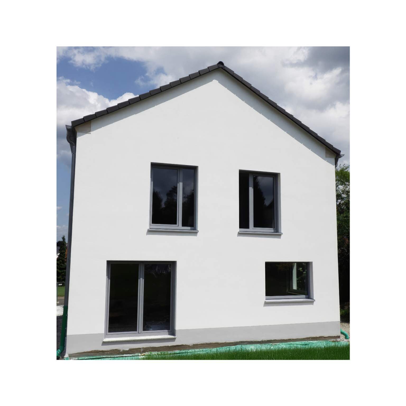 Zeitloses Massivhaus mit grauen Fensterrahmen und klaren Linien im Neubaugebiet.