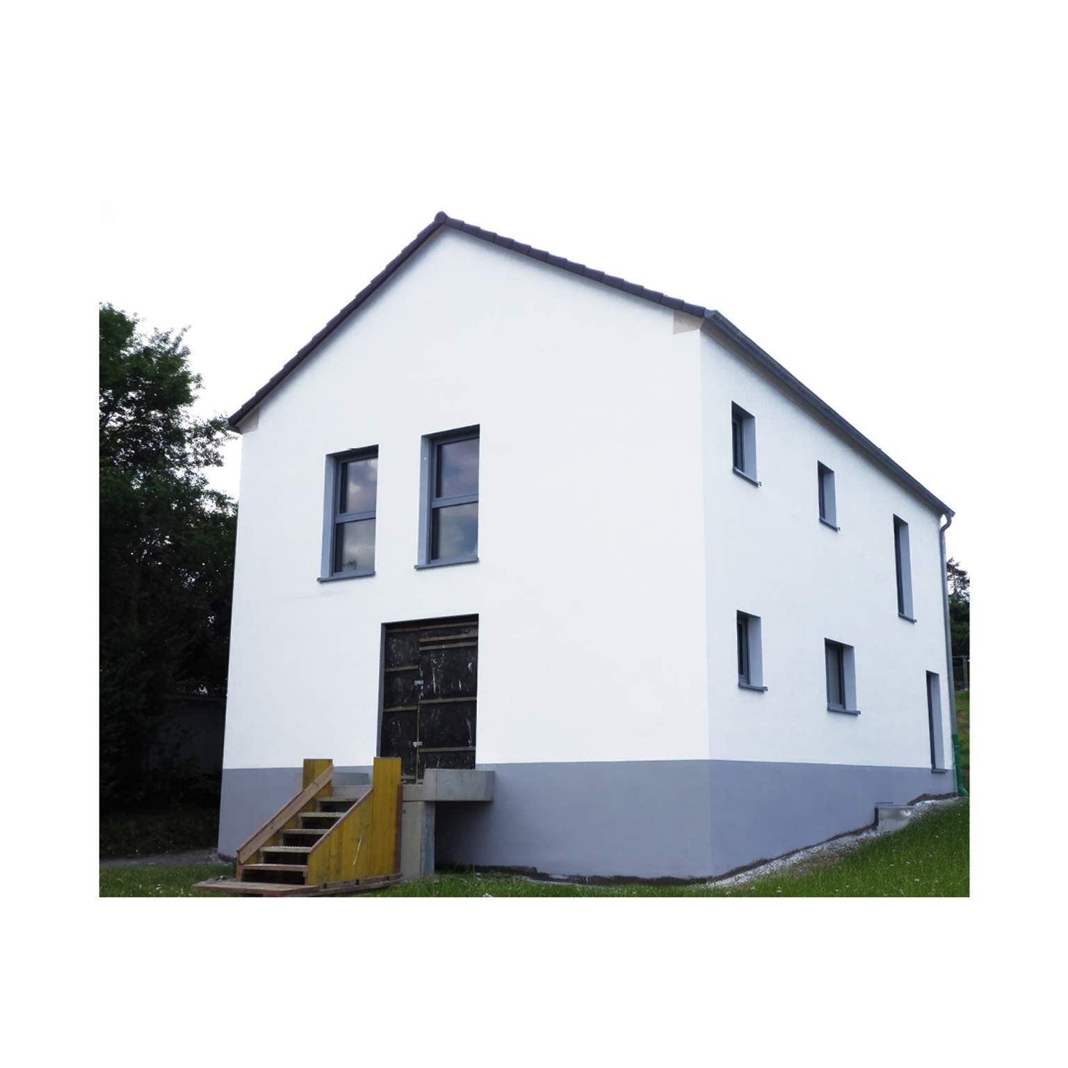 Kompaktes Einfamilienhaus mit dunklem Sockel und Treppenaufgang zum Eingangsbereich.