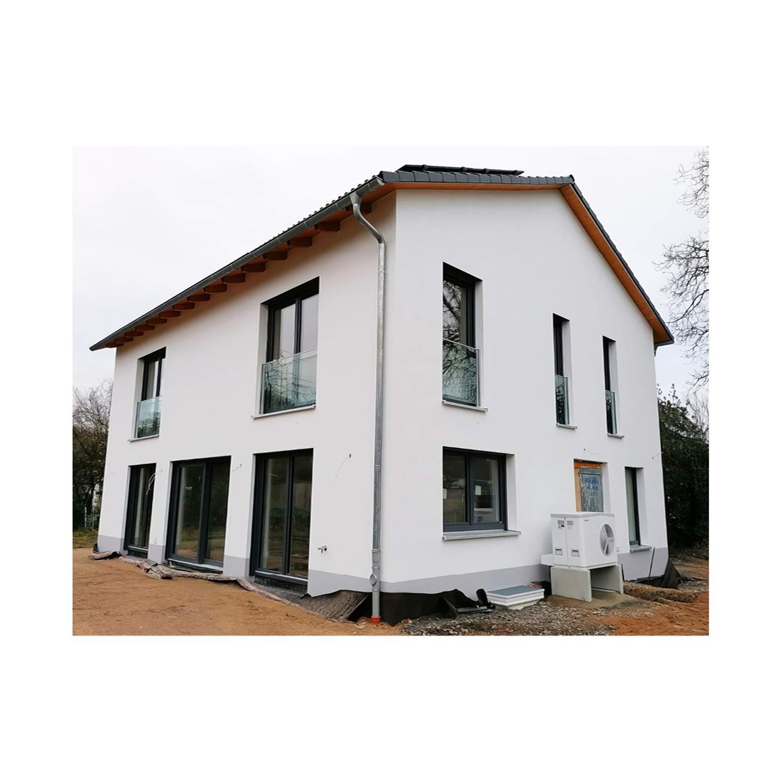 Zweigeschossiges Einfamilienhaus mit Satteldach, moderner Luft-Wärmepumpe und anthrazitfarbenen Fensterrahmen für energieeffizientes Bauen 2026.